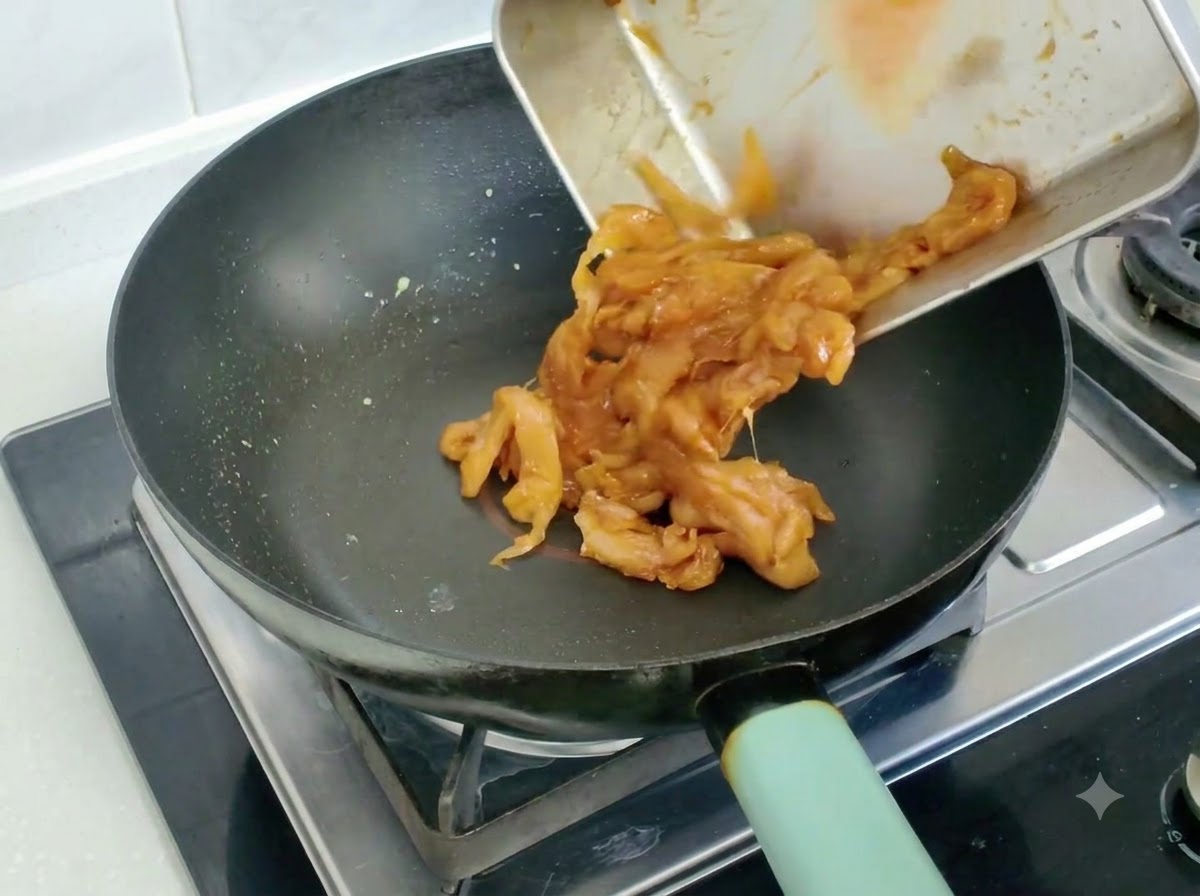 Marinierte Hähnchenstücke werden in eine Bratpfanne gegeben und angebraten.