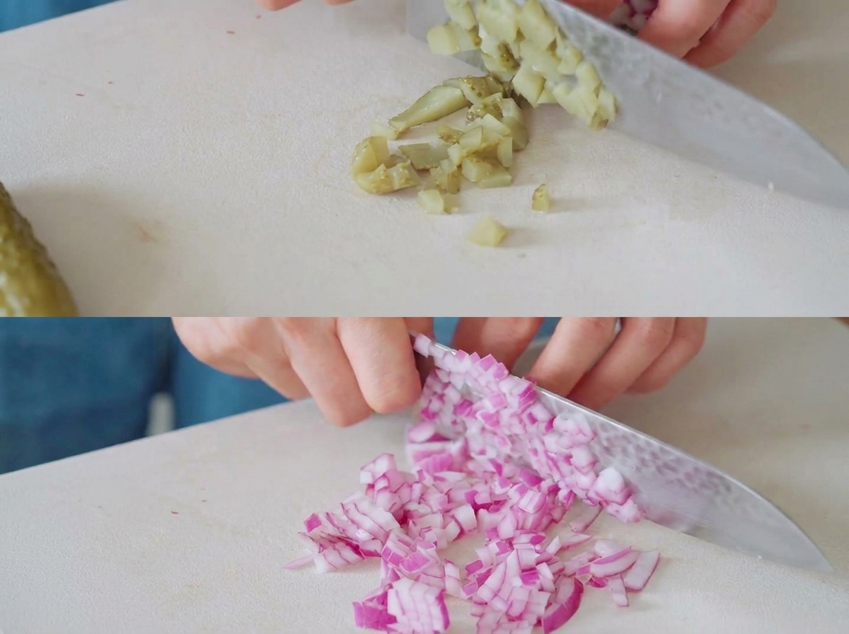 Essiggurken und rote Zwiebeln werden mit einem Kochmesser auf einem weißen Schneidebrett in kleine Stücke geschnitten.