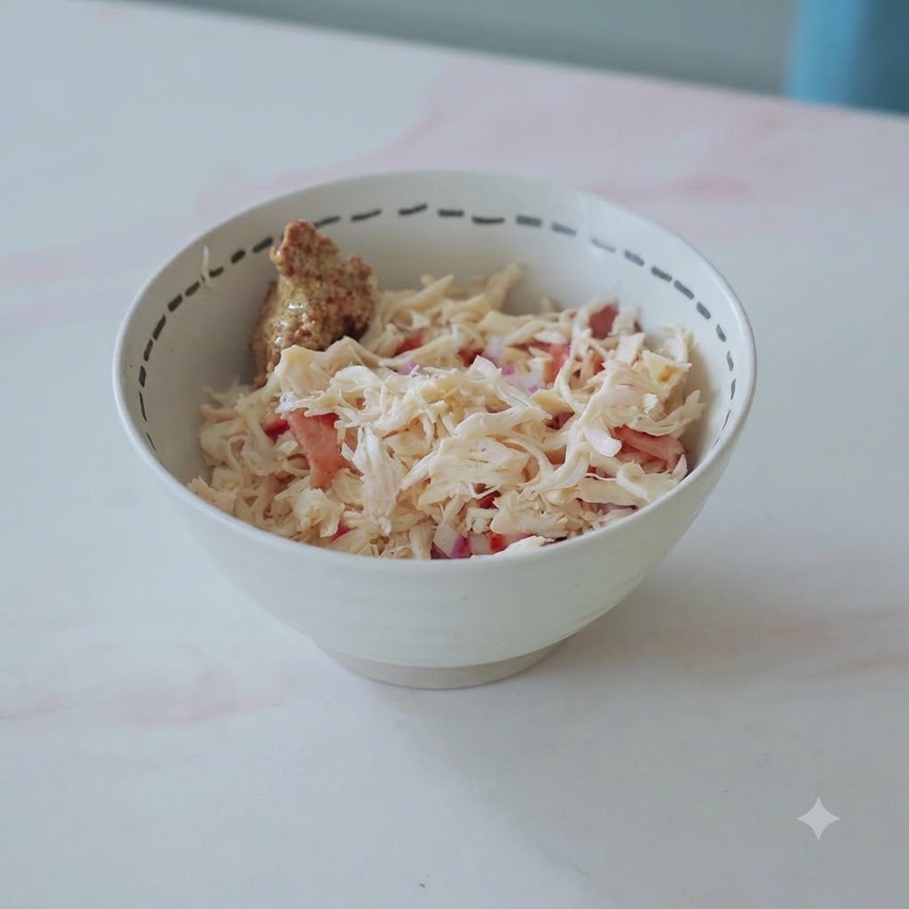 Eine Schüssel gefüllt mit gezupftem Hähnchen, Speck, Zwiebeln und einem Klecks Senf, bereit zum Vermengen.