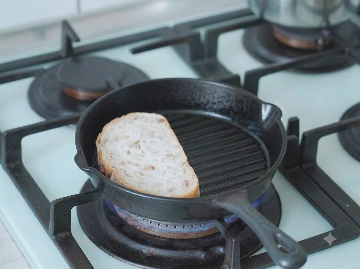 Eine Scheibe Sauerteigbrot toastet in einer heißen Gusseisen-Grillpfanne auf dem Herd.