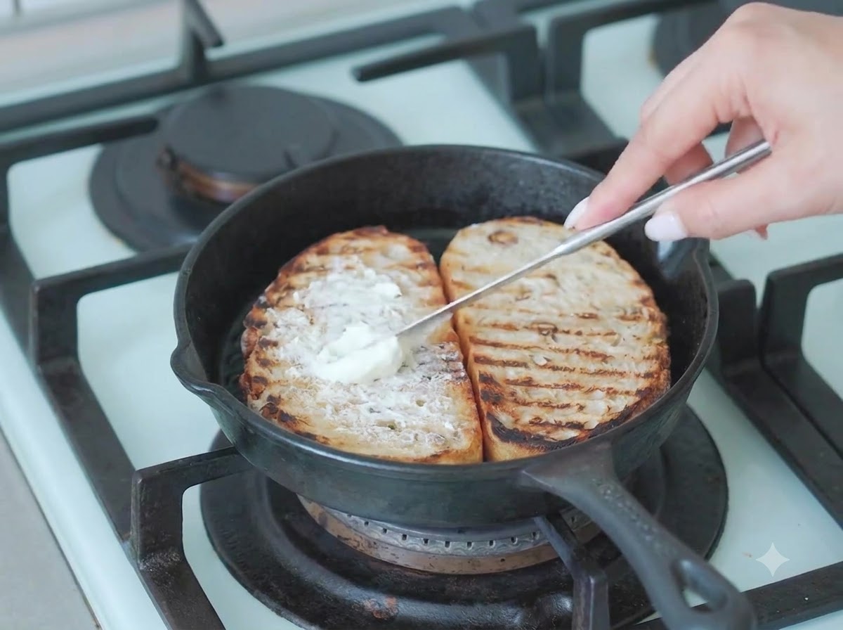 Frische grüne Rucolablätter werden oben auf die Frischkäseschicht auf dem Sauerteigbrot gelegt.