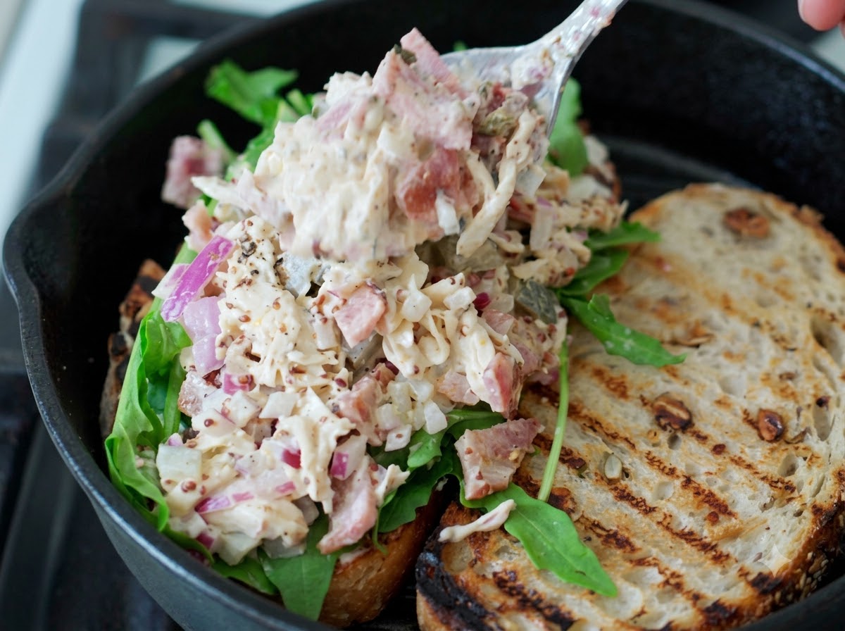 Ein Löffel gezupfter Hähnchen-Salat wird auf den frischen grünen Rucola auf einer Sauerteig-Sandwichscheibe gegeben.