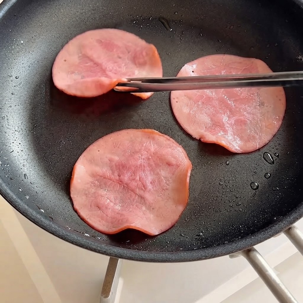 Schinkenscheiben werden mit Stäbchen in einer Bratpfanne gewendet.