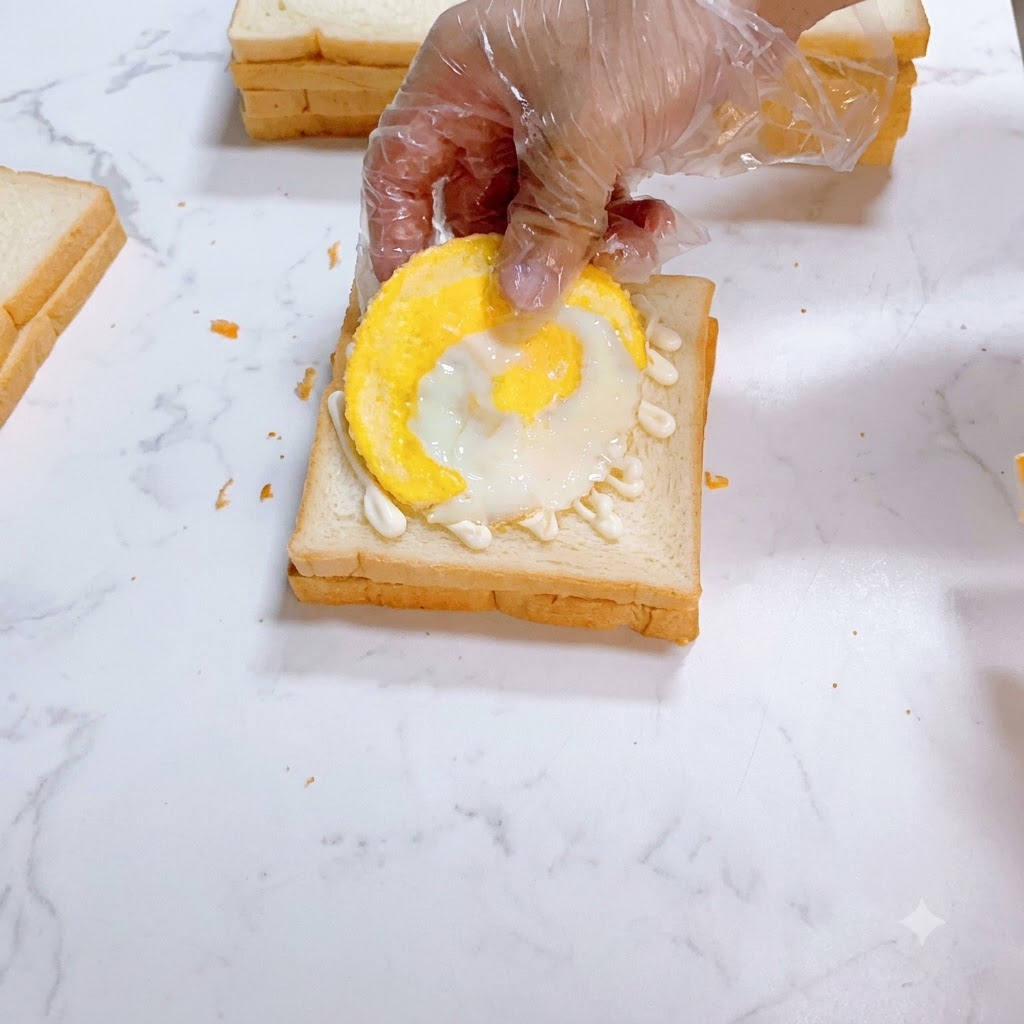 Ein Spiegelei wird sorgfältig auf mit Mayonnaise bestrichenem Weißbrot platziert.