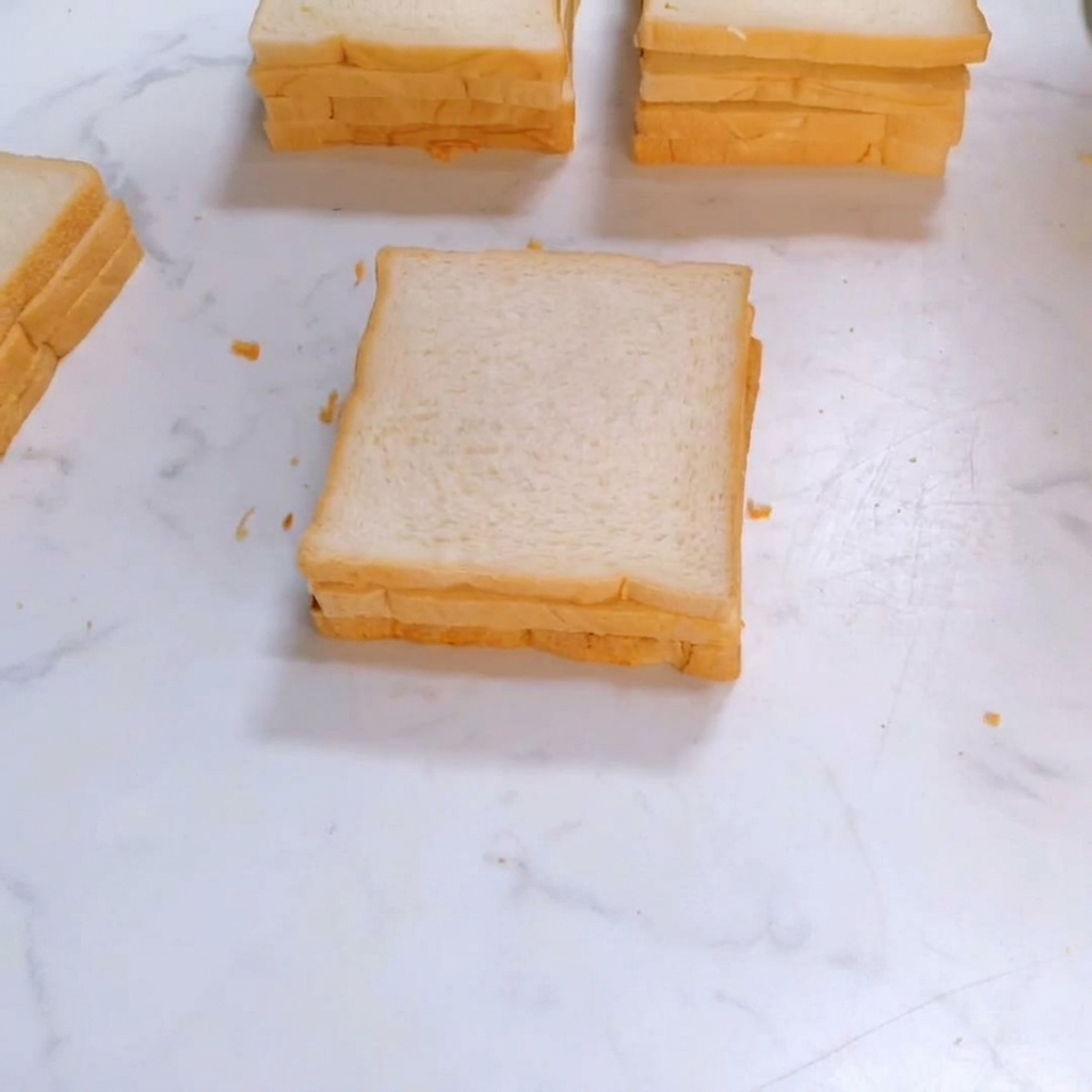 Eine dritte Scheibe quadratisches Weißbrot wird auf den Sandwich-Stapel gelegt.