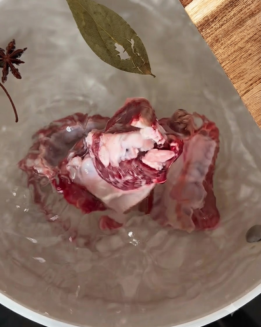 Schweinerippchen in einem Topf mit Wasser, in dem Sternanis und ein Lorbeerblatt schwimmen.