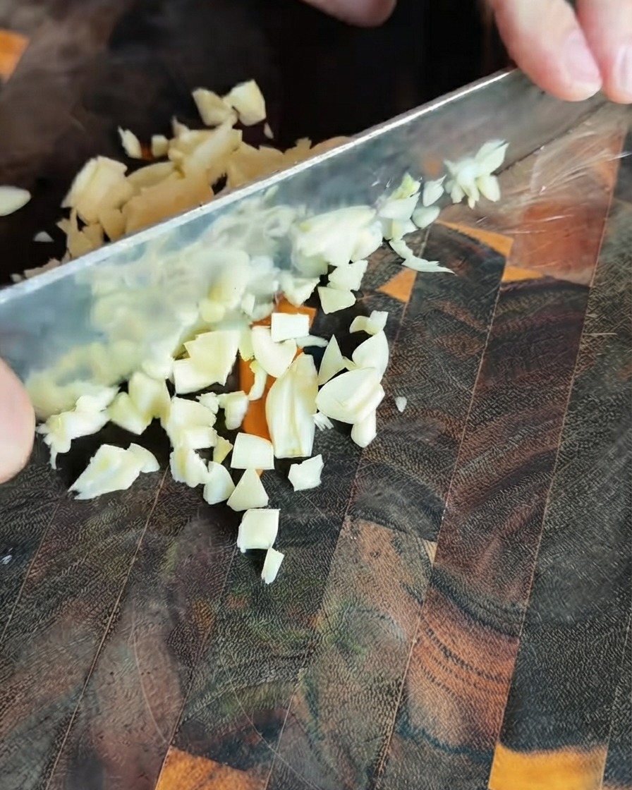 Frisch gehackte Knoblauchstückchen auf einem dunklen Holzschneidebrett.