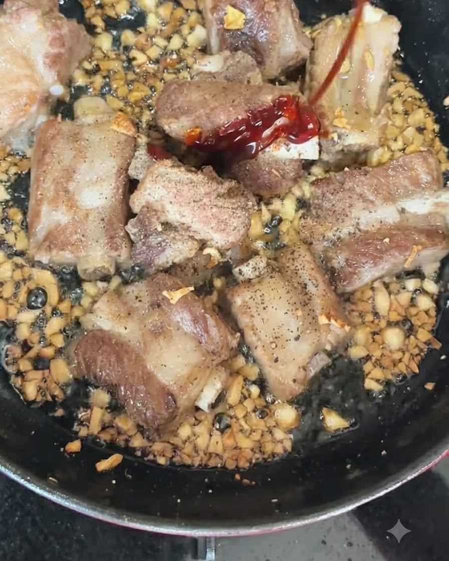 Rote und grüne Chilis werden in eine heiße Pfanne mit anbratenden Schweinerippchen und gehacktem Knoblauch gegeben.