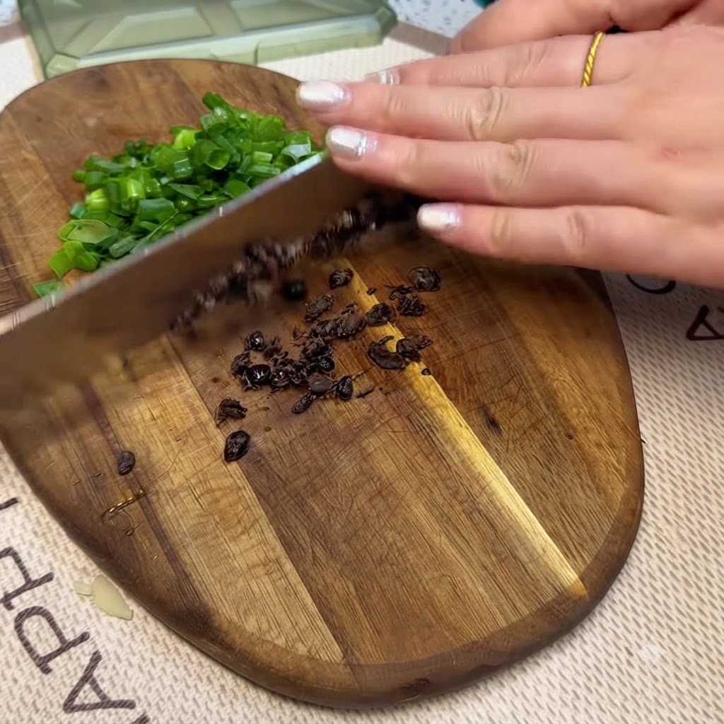 Fermentierte schwarze Bohnen und gehackte Frühlingszwiebeln werden auf einem Holzschneidebrett mit einem Messer zerkleinert.