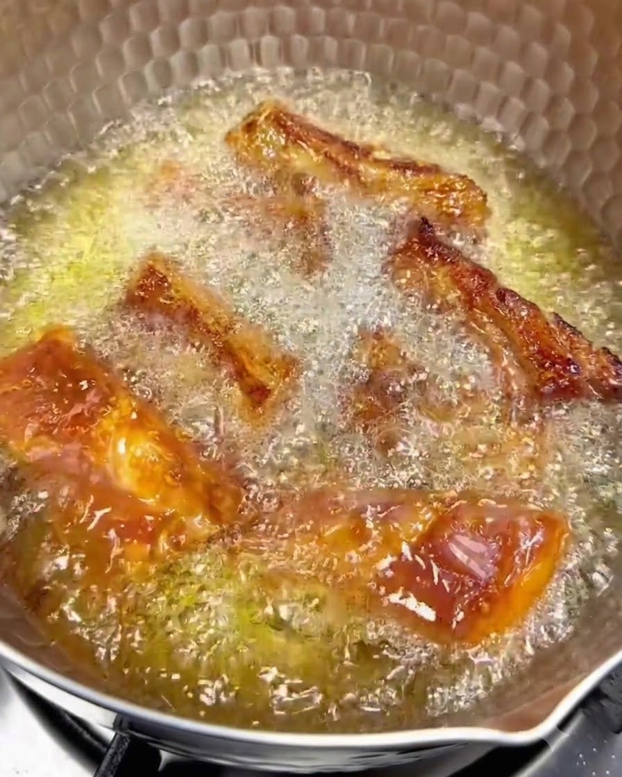 Schweinerippchen braten bei schwacher Hitze in heißem Öl, wobei die goldbraunen Oberflächen sichtbar sind.