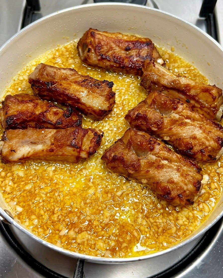Goldbraun gebratene Schweinerippchen liegen ordentlich in einer Pfanne voller köchelnder Knoblauch-Buttersauce.