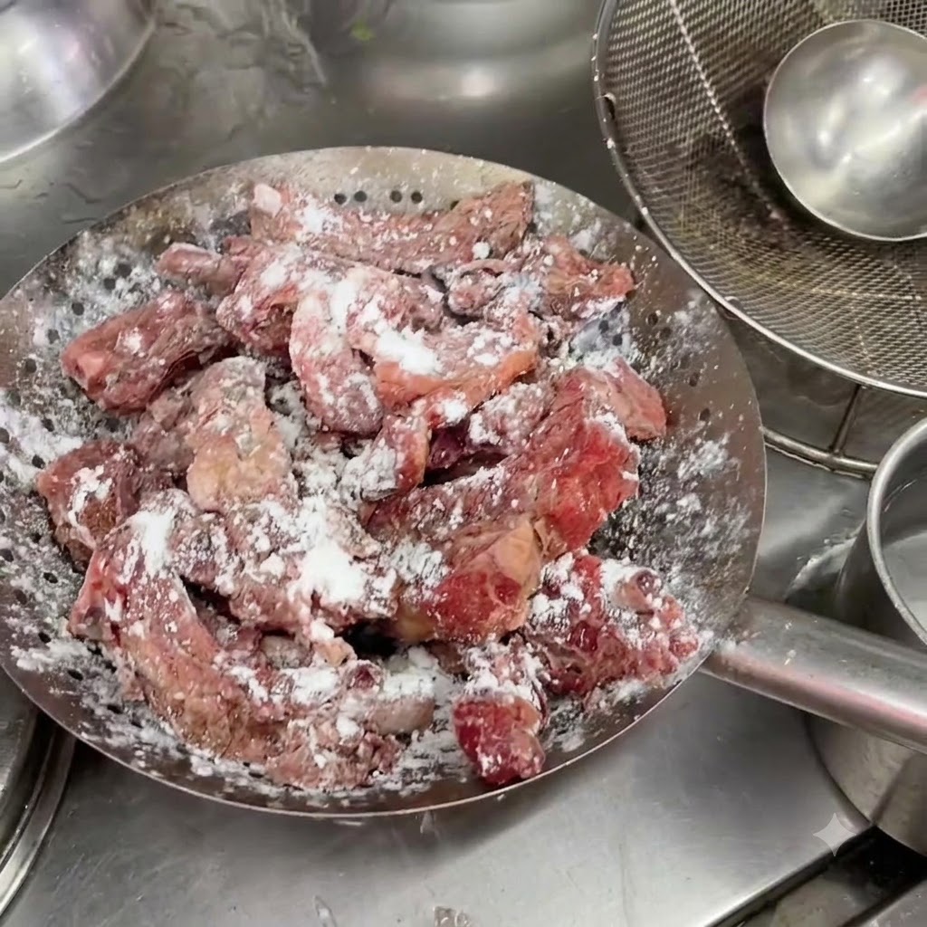 Marinierte Schweinerippchen in einem Metallsieb mit einer sichtbaren weißen Stärkeschicht.