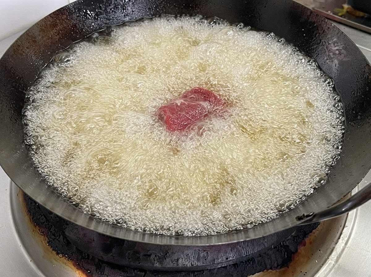Ein einzelnes Schweinerippchenstück wird in einen mit kochend heißem Frittieröl gefüllten Wok gegeben.