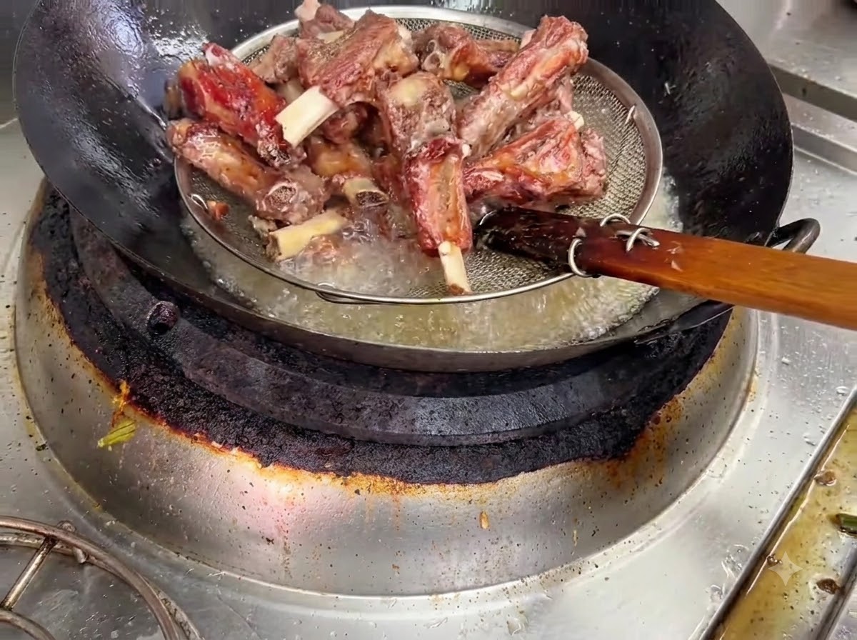 Frittierte Schweinerippchen werden mit einem Drahtsiebkorb aus dem heißen Öl gehoben.