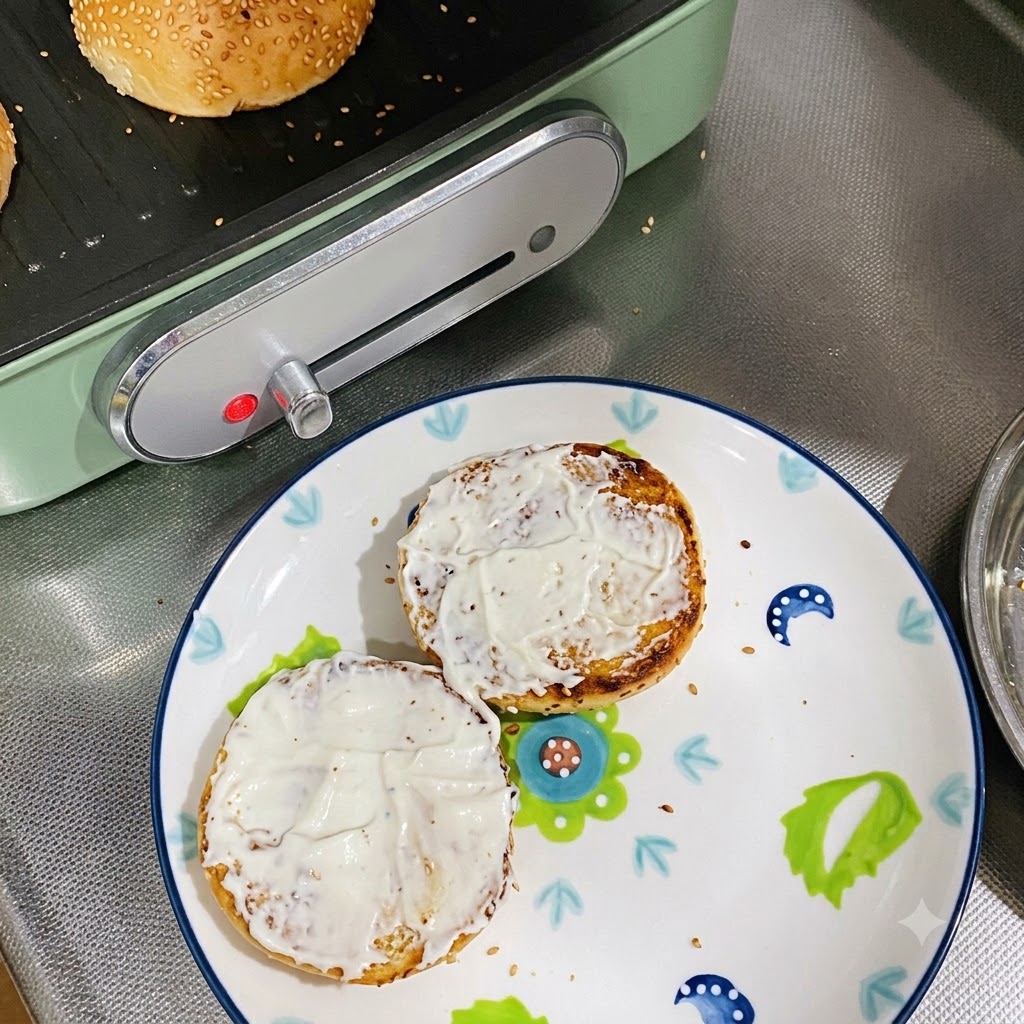 Zwei mit Mayonnaise bestrichene Brötchenhälften auf einem dekorierten Teller.