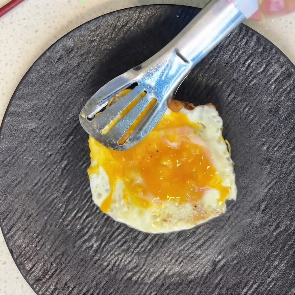 Ein frisch gebratenes Spiegelei wird mit einer Metallzange sorgfältig auf Tomatenscheiben positioniert.