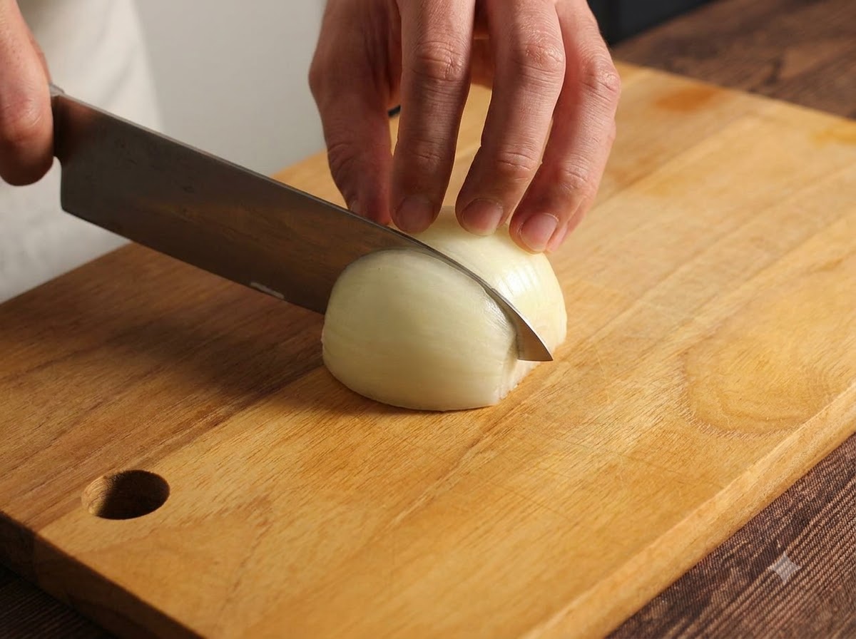 Eine Zwiebel wird auf einem Holzschneidebrett mit einem Küchenmesser sorgfältig gehackt und fein gewürfelt.