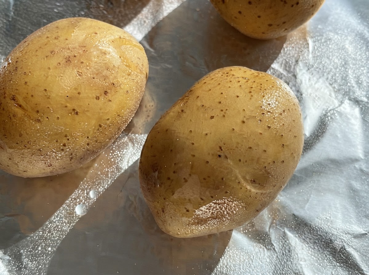 Rohe ganze Kartoffeln, bestrichen mit Öl, auf einem Stück Alufolie.