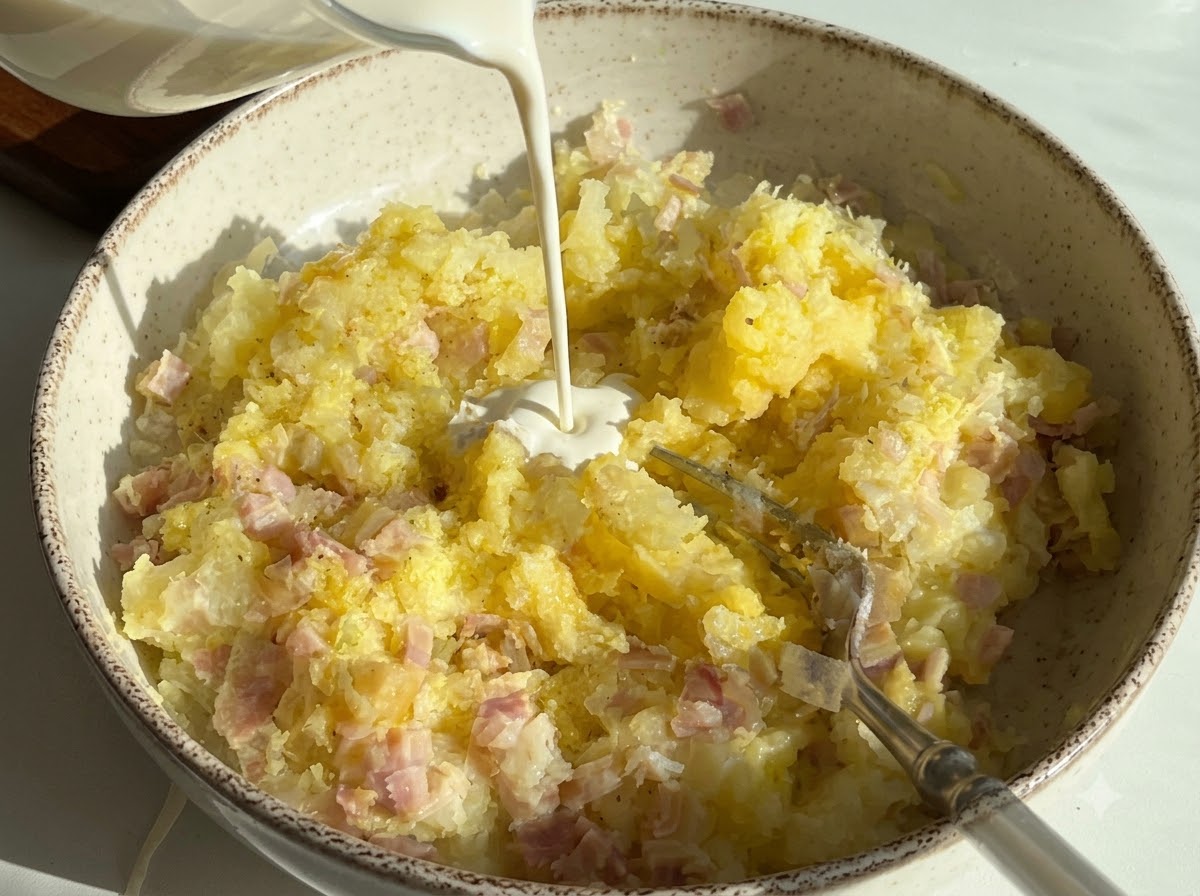 Schlagsahne wird in eine Schüssel mit Kartoffelpüree und Schinkenstückchen gegossen.
