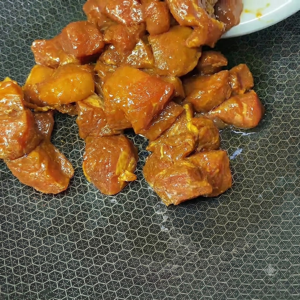 Marinierte, rotbraune Schweinefleischwürfel garen in einem heißen, strukturierten Wok.