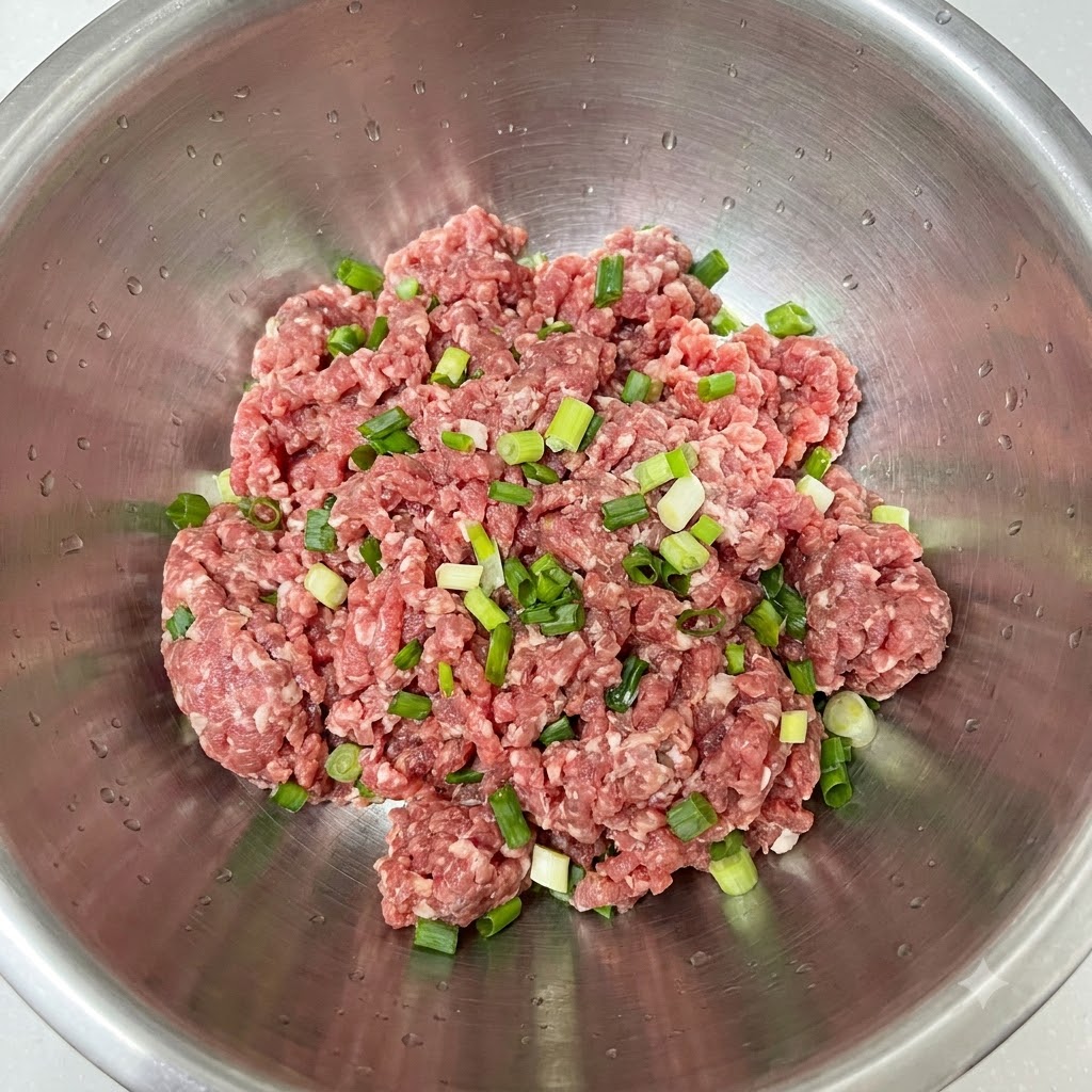 Frisch gehackte Frühlingszwiebeln auf Hackfleisch in einer Edelstahlschüssel.