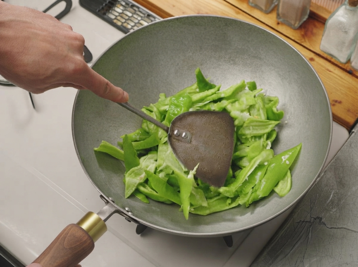 Geschnittene grüne Paprika wird mit einem Metallspatel in einem heißen, trockenen Wok geschwenkt.
