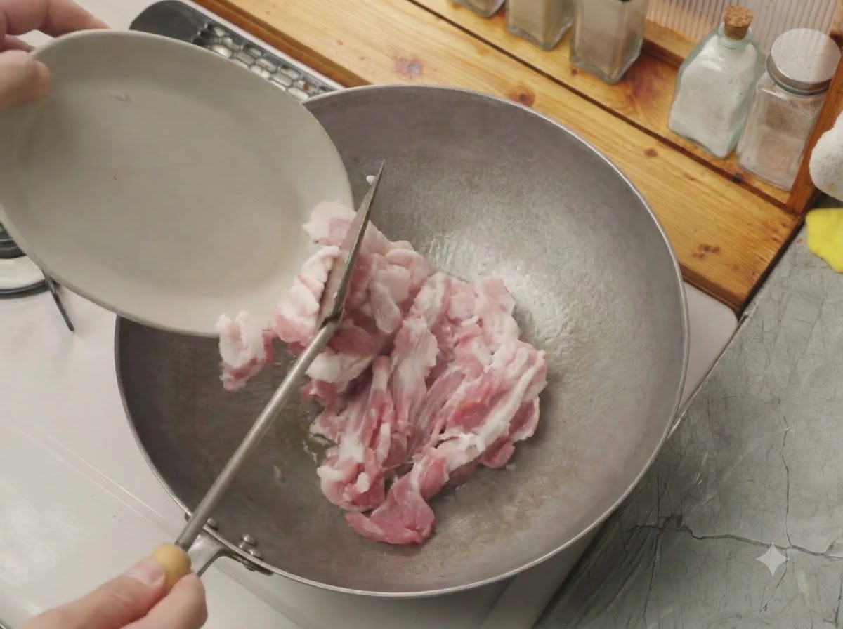 Rohe Schweinebauchscheiben werden von einem kleinen weißen Teller in einen heißen Wok gekippt.