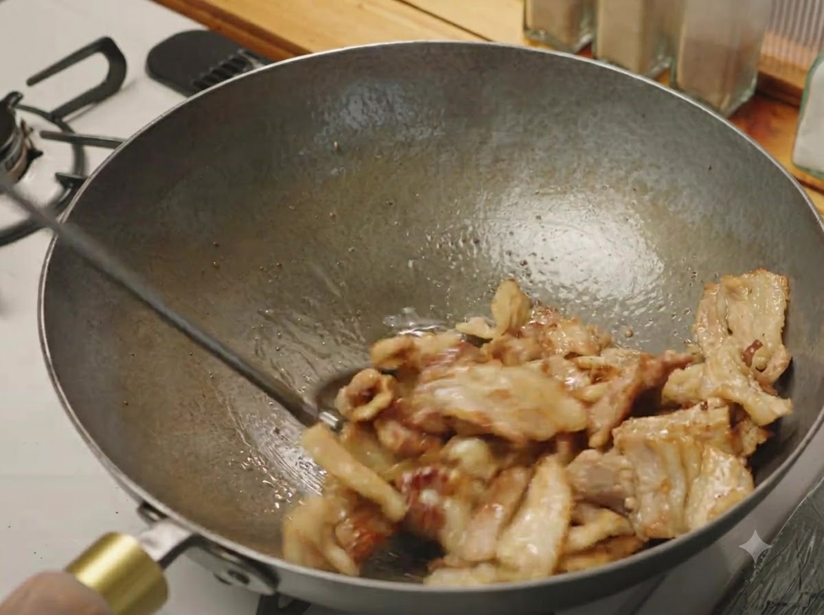 Schweinebauchscheiben werden in einem Wok unter Rühren gebraten, bis sie leicht gebräunt sind und brutzeln.