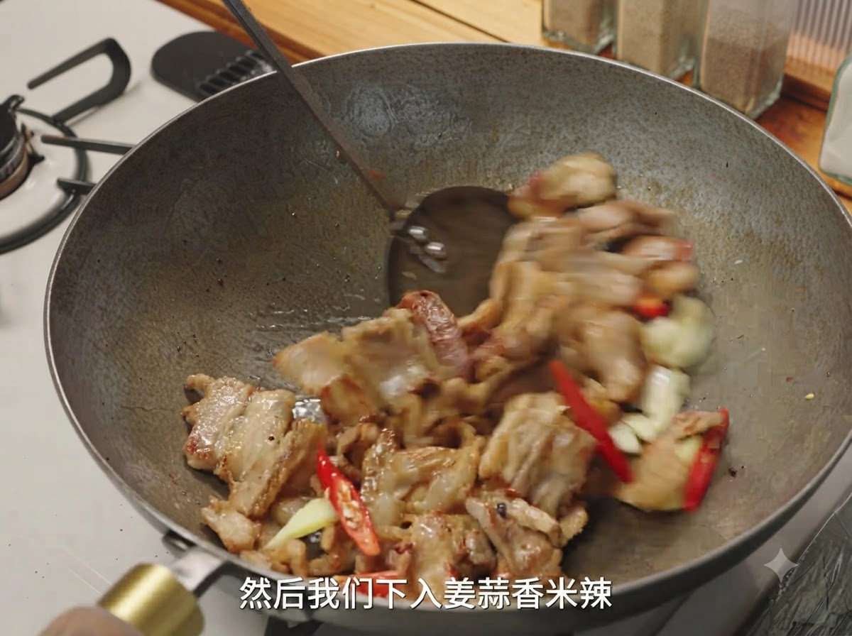 Ingwer, Knoblauch und rote Chilis werden zusammen mit gebräunten Fleischstücken in einem Wok geschwenkt.
