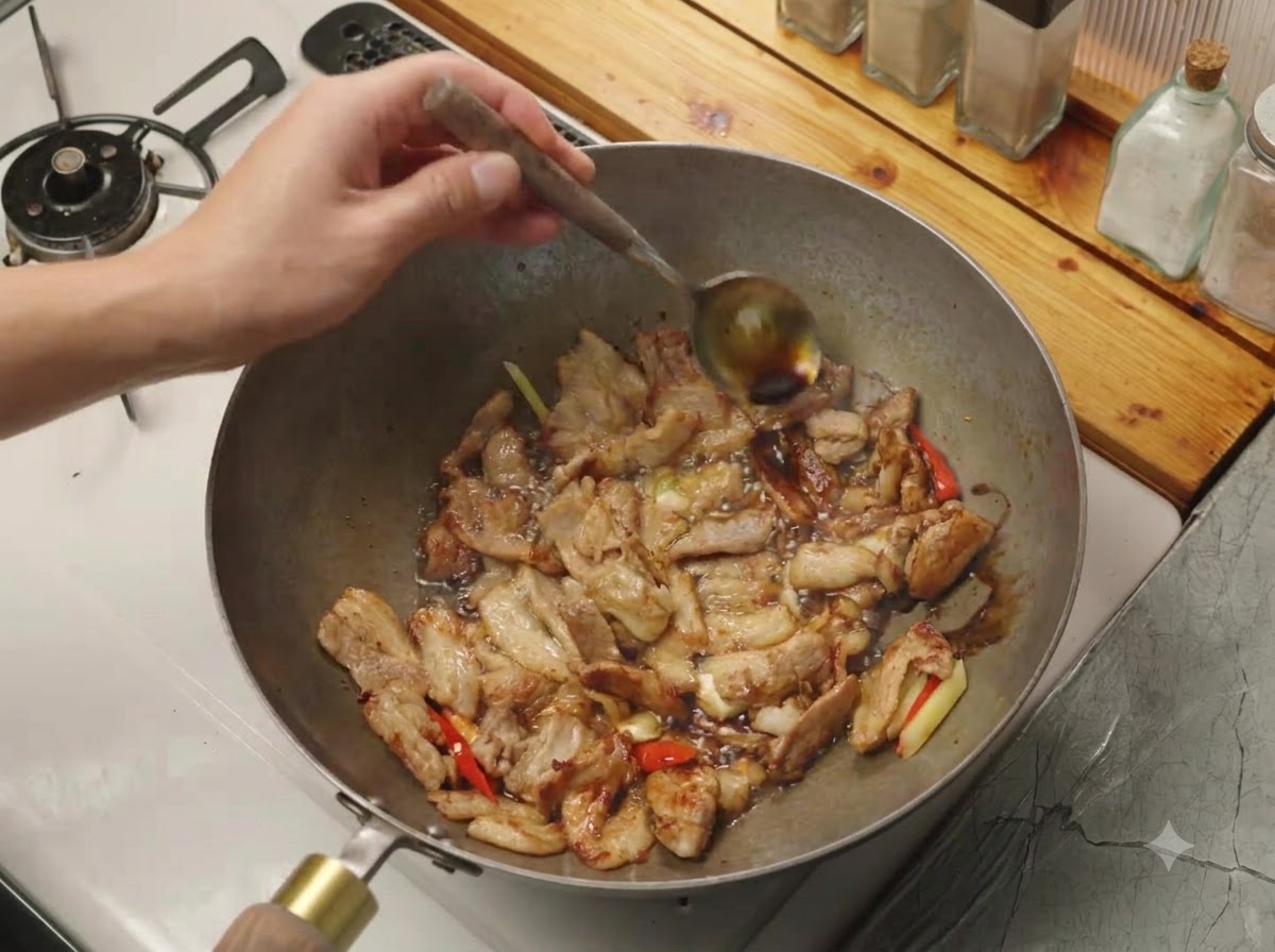 Sojasauce wird von einem Löffel an den heißen Rand eines Woks mit Fleisch und Aromaten gegossen.
