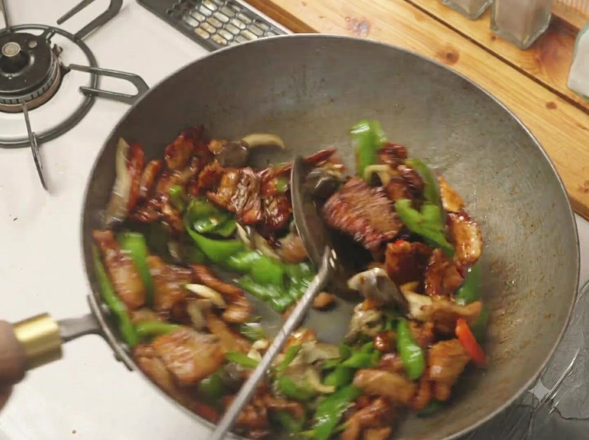 Ein Spatel mischt grüne Paprika, Pilze und Schweinebauch in einem heißen Wok zusammen.