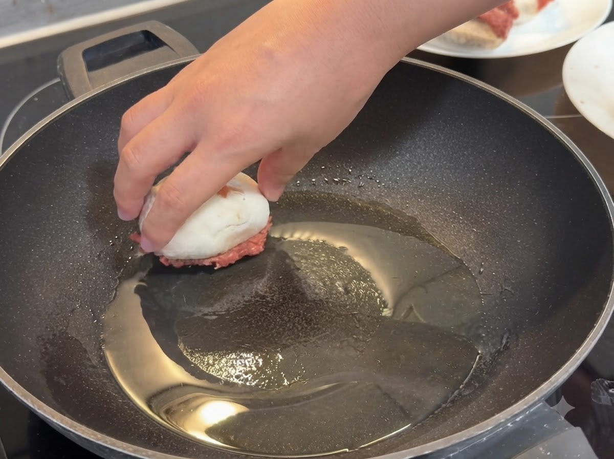 Eine Hand platziert einen gefüllten Champignon mit der Fleischseite nach unten in eine heiße, geölte Pfanne.