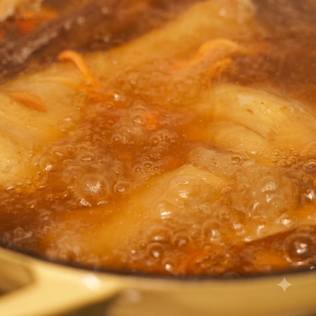 Nahaufnahme von Nudeln und Gemüse, die in blubbernder Brühe kochen.