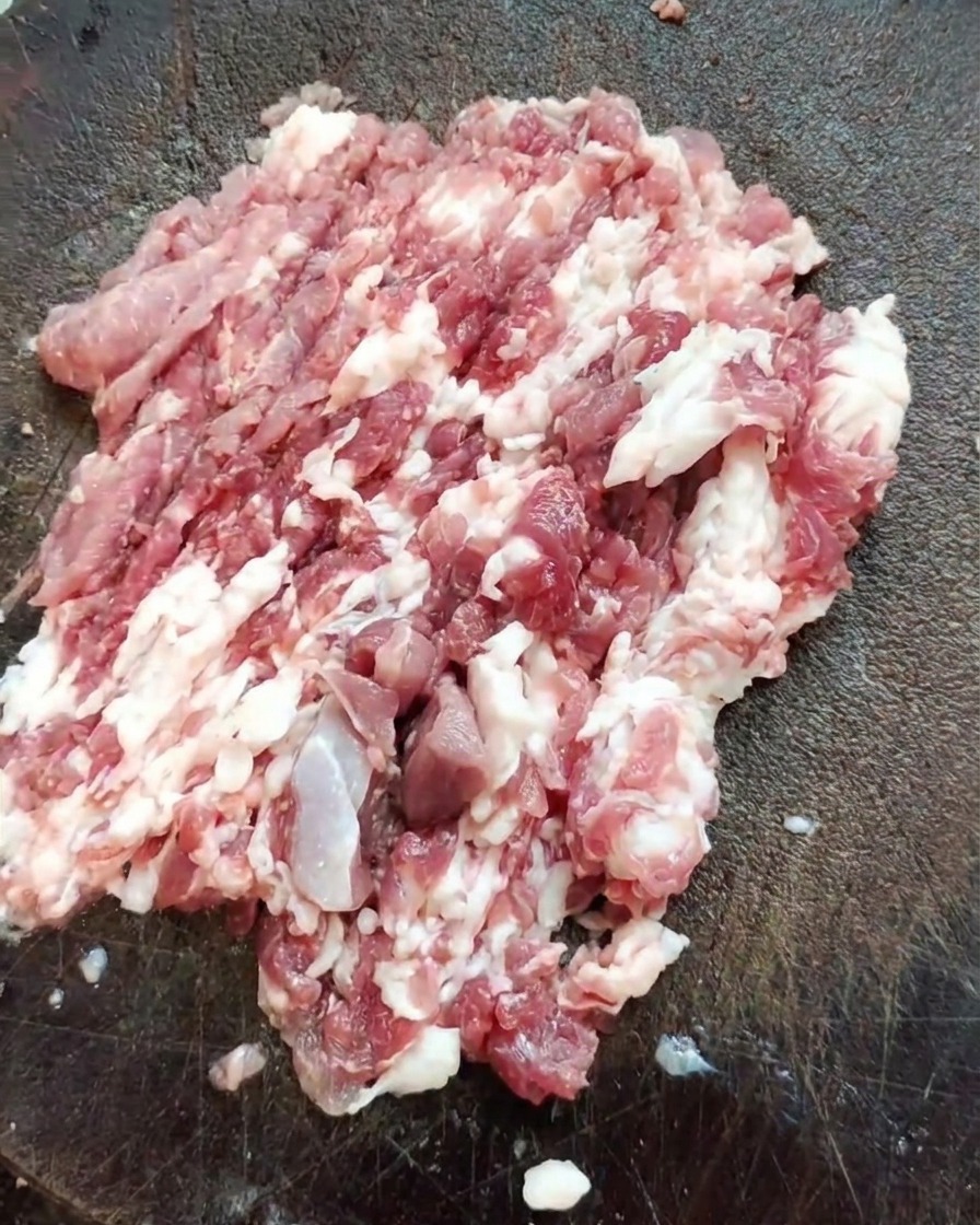 Ein scharfes Beil auf einem Haufen frisch gehacktem Schweineschulterfleisch auf einem strukturierten Holzbrett.