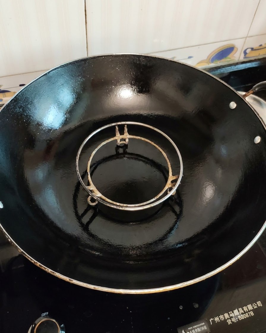 Ein leerer Dämpfereinsatz in einem großen schwarzen Wok, bereit zum Kochen.