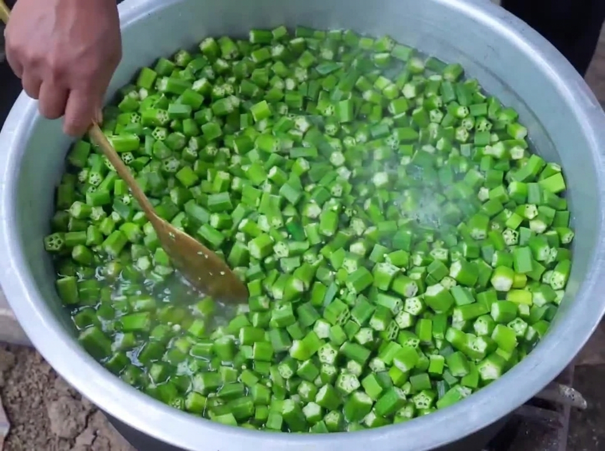 Gehackte grüne Okra wird in kochendem Wasser in einem großen Topf blanchiert und mit einem Holzlöffel umgerührt.