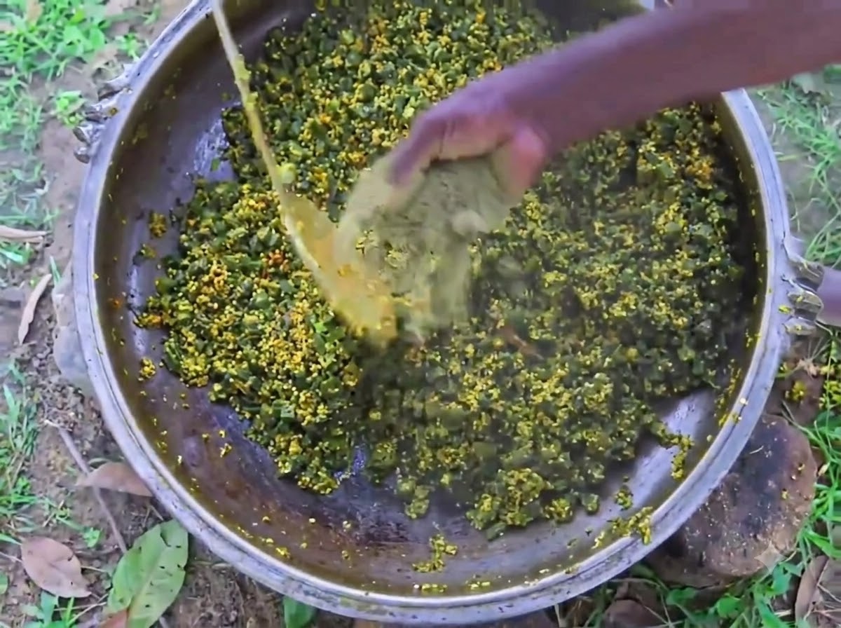 Die Hand einer Person mischt schwarzen Pfeffer in Pulverform in einen großen Eisernen Topf mit kochender Okra und Eiern.