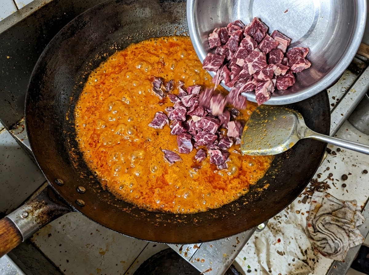 Stücke von Rinderbrust werden aus einer Metallschüssel in eine blubbernde rote Chiliöl-Mischung in einem Wok gegeben.