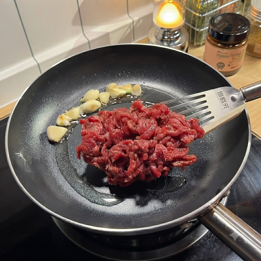 Gewürzte rohe Rinderstreifen werden mit einem Pfannenwender in eine heiße Pfanne mit angebratenem Knoblauch gegeben.