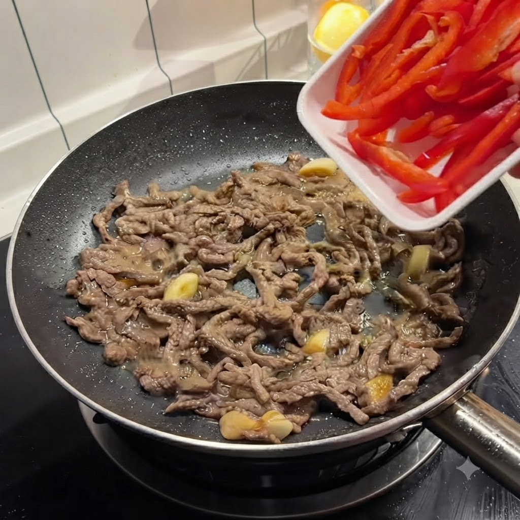 Rote Paprikastreifen werden aus einer weißen Schale in eine Bratpfanne mit angebratenem Rindfleisch geschüttet.