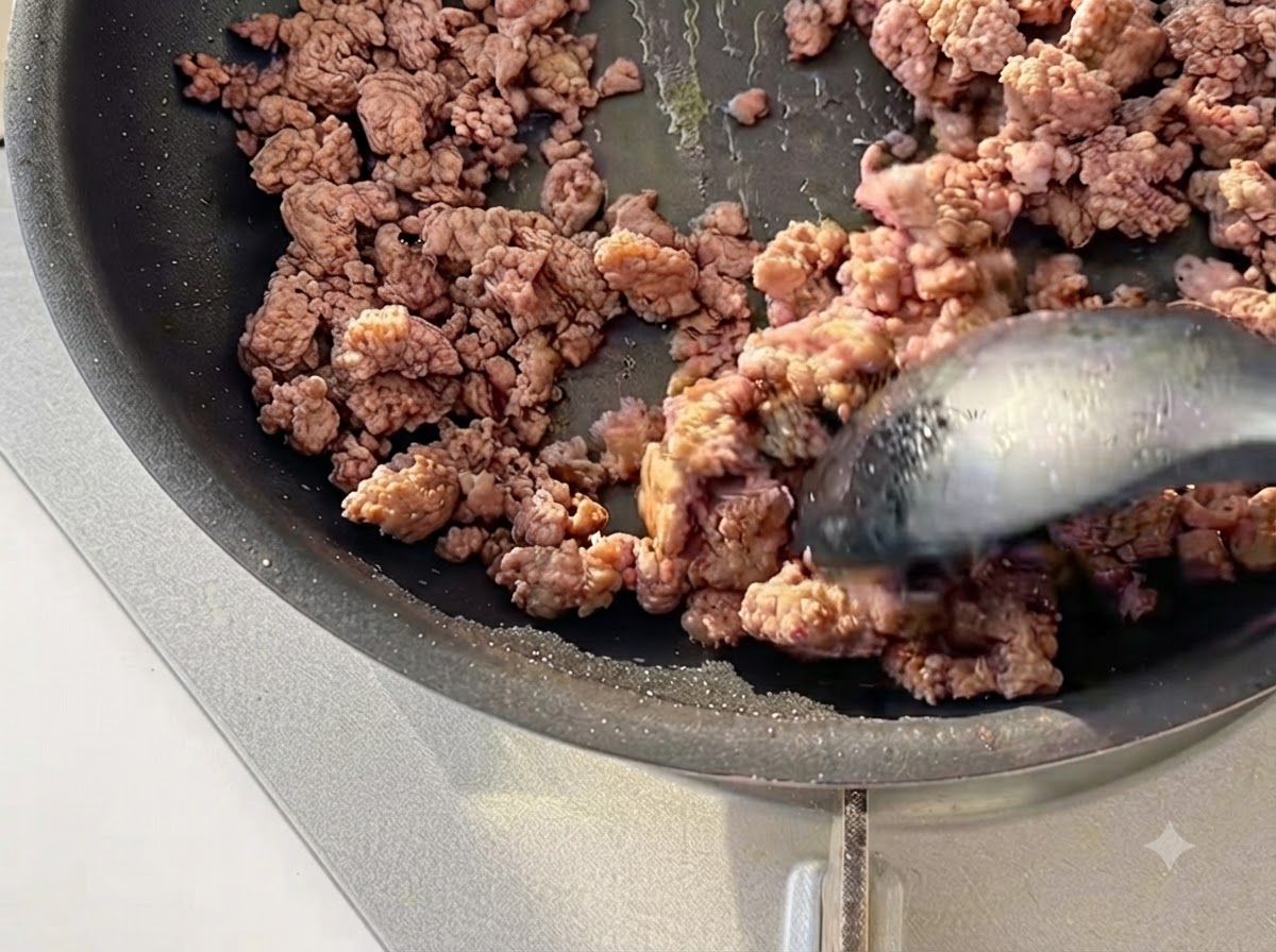 Hackfleisch wird mit einem Spatel in einer schwarzen Pfanne leicht gebräunt und angebraten.