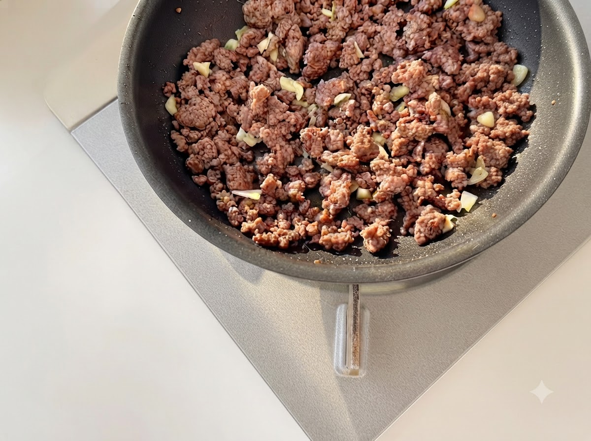 Minimierter Knoblauch und gewürfelte Tomaten werden zusammen mit gebräuntem Hackfleisch in einer Pfanne angebraten.