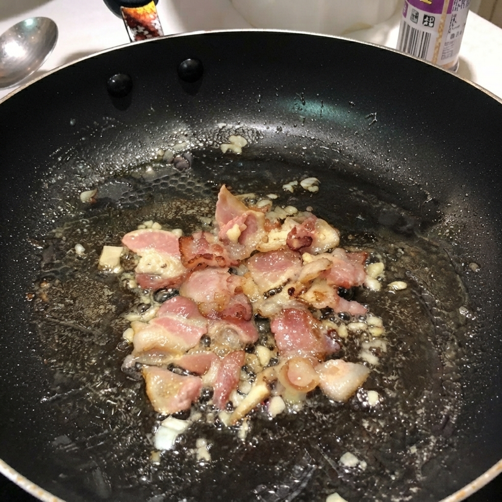 Gekochte Penne-Nudeln vermischt mit Bacon und Zwiebeln in einer schwarzen Bratpfanne.