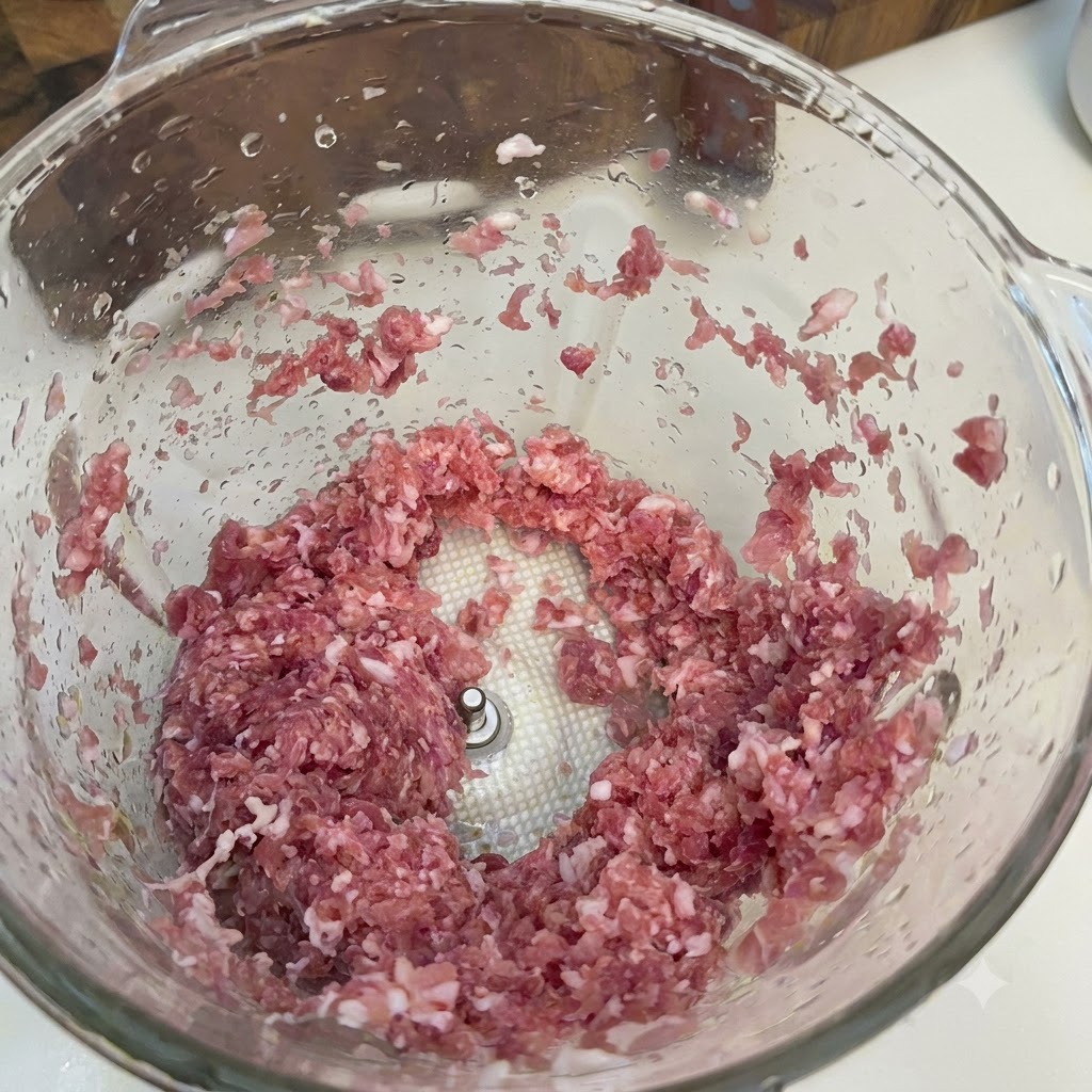 Stücke von Schweine- oder Rindfleischhack in einer Glas-Küchenmaschinenschüssel.