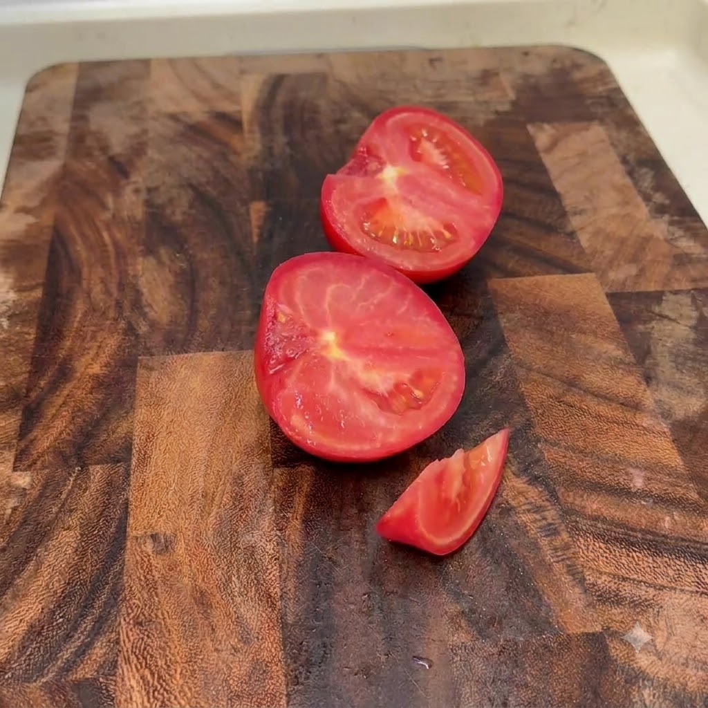 Frische Tomaten in Hälften und kleine Stücke geschnitten auf einem Holzschneidebrett.