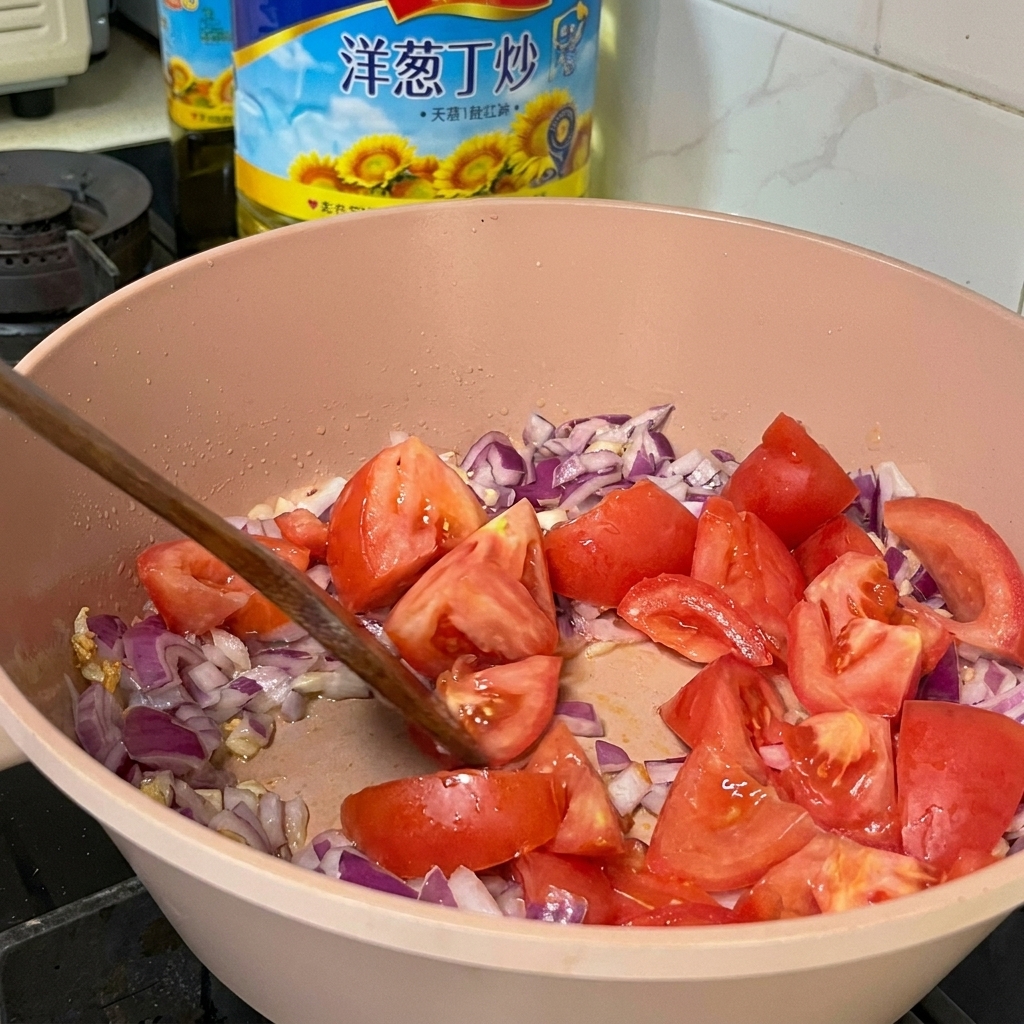 Frische Tomatenstücke werden mit gewürfelten roten Zwiebeln und Knoblauch in einer rosa Kochpfanne mit einem Holzwender vermischt.