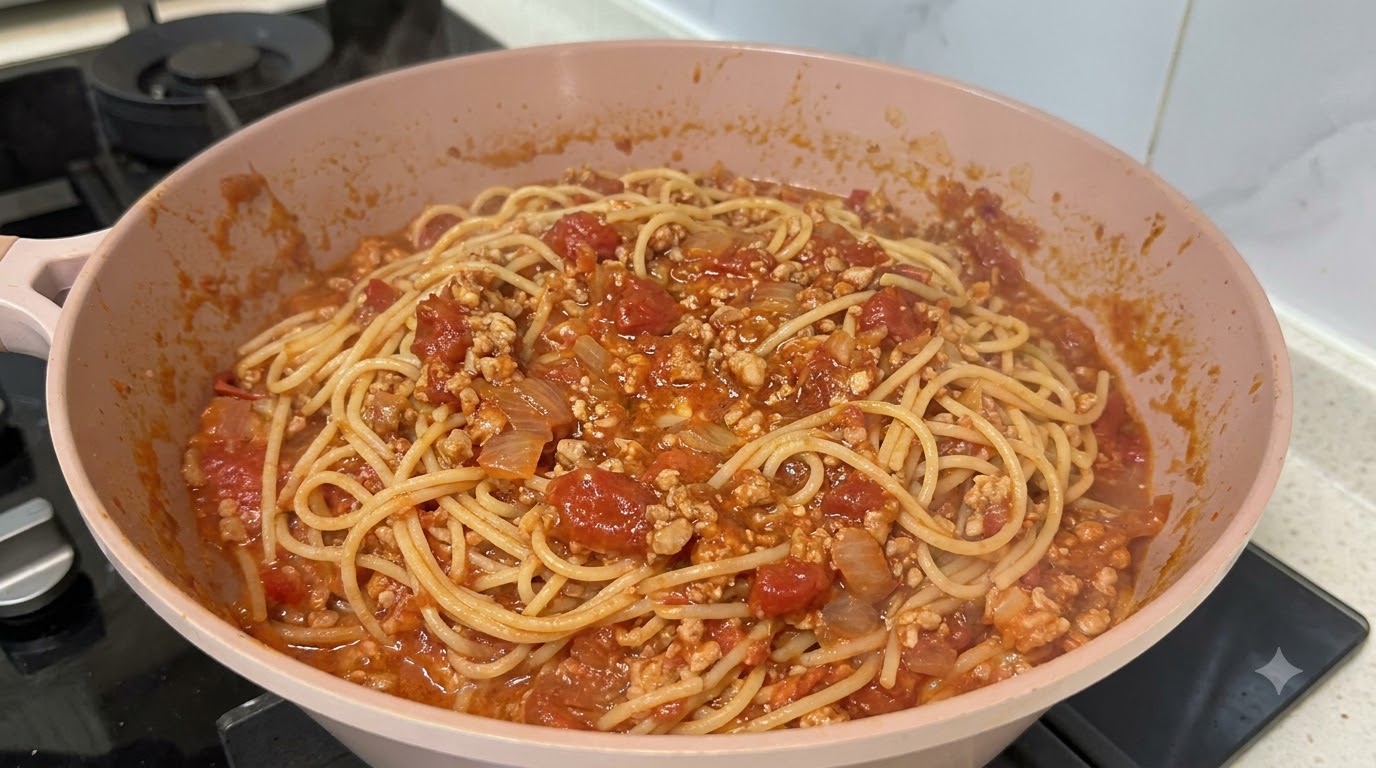 Frisch gekochte Spaghetti vermengt mit einer reichhaltigen, stückigen roten Bolognese-Hackfleischsauce in einer rosa Pfanne.
