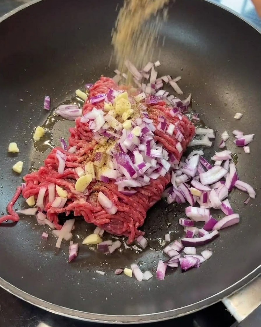 Gewürze werden über Hackfleisch und Zwiebeln in einer Bratpfanne gestreut.