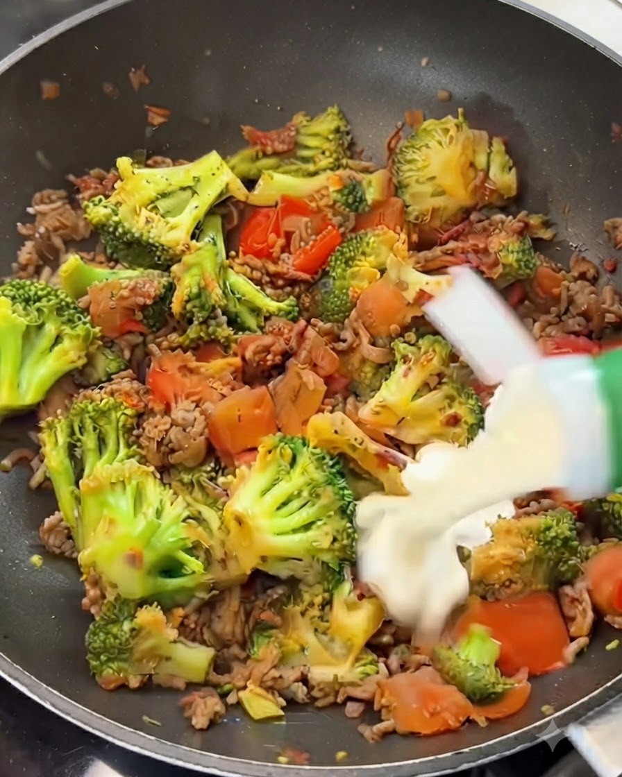 Sahne wird aus einem Tetrapak über eine Mischung aus Rindfleisch, Brokkoli und Tomaten in einer Pfanne gegossen.