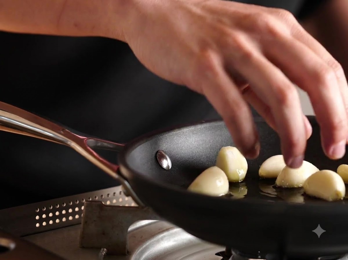 Ganze geschälte Knoblauchzehen werden in eine Pfanne mit Olivenöl gegeben.